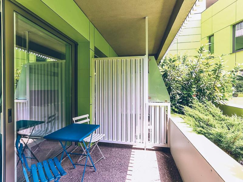 Balcony with blue table and chairs next to a green building and plants.
