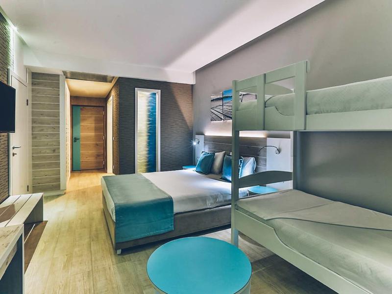 Modern hotel room with double bed and bunk bed, simple decor in neutral tones.