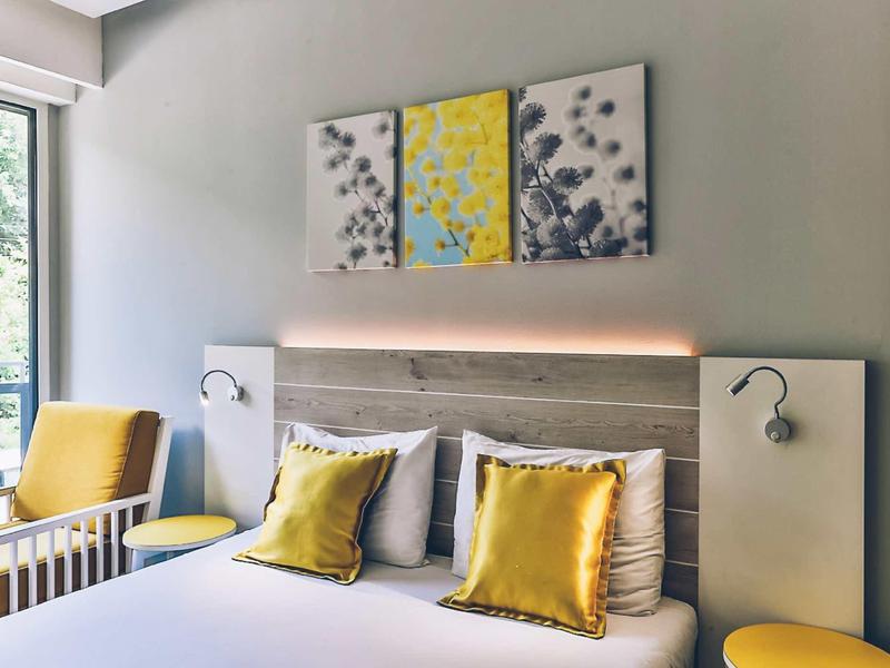 Modern hotel room with double bed, yellow accent pillows, and abstract wall art.