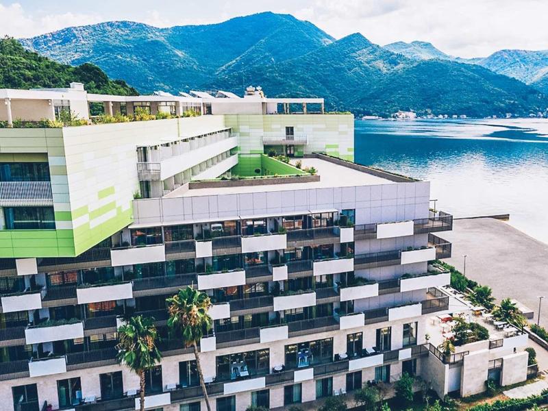 Modern hotel by the lake with panoramic mountain and beach views in the background.