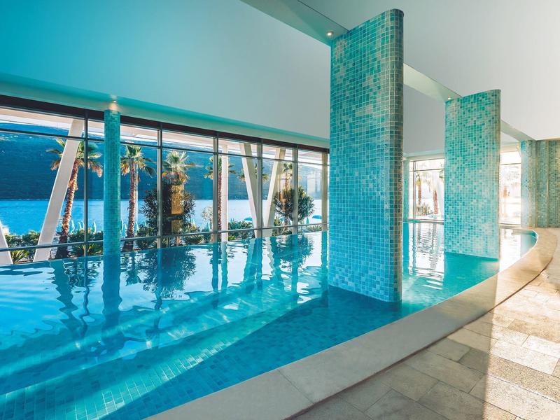 Modern indoor pool with large windows overlooking palm trees in sunlight