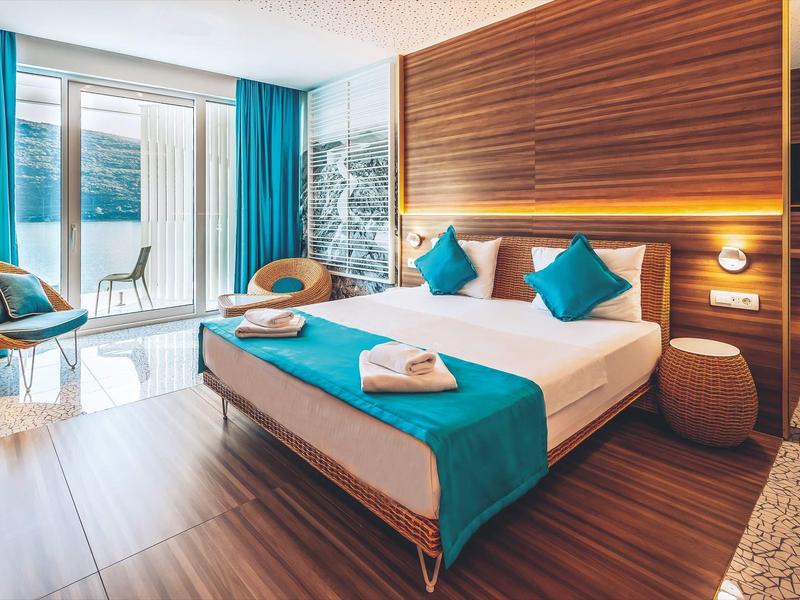 Hotel room with double bed, turquoise accents, and balcony with sea view
