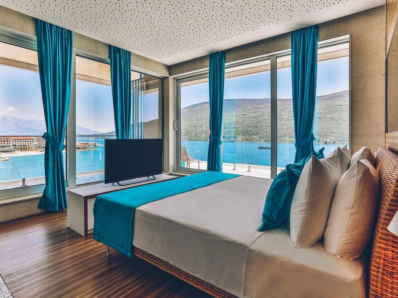 Modern hotel room with large bed, blue decor, and sea view through large windows.
