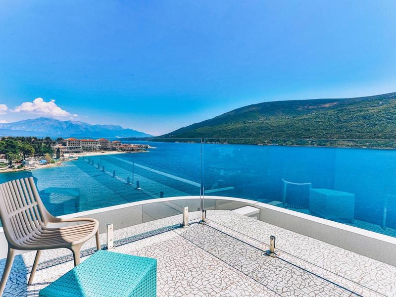 Terrace with modern seating and glass railing overlooking the sea and mountains