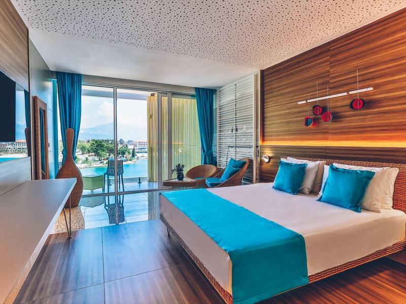 Modern hotel room with double bed, blue accents, and balcony with sea view.