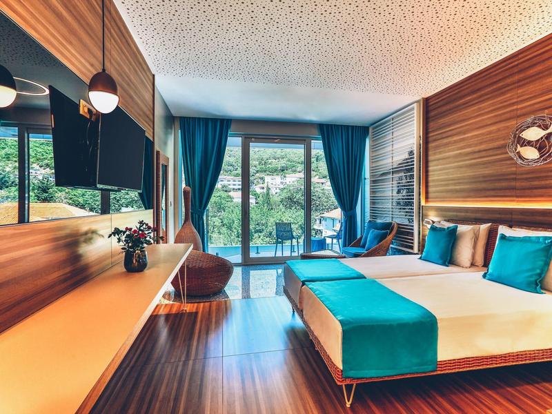 Modern hotel room with wood accents, blue-turquoise highlights, and large window overlooking greenery