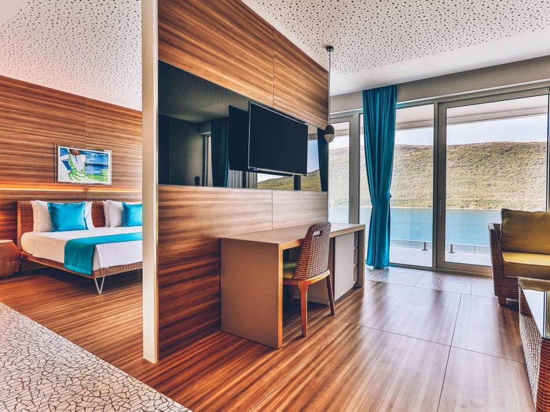 Modern hotel room with bed, desk, TV, and access to a terrace.