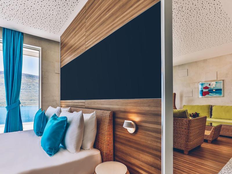 Modern hotel room with a large bed, blue curtains, and a living area with a green sofa.