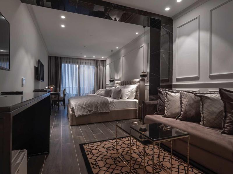 Modernes Schlafzimmer mit grauer Wandgestaltung, Doppelbett, Teppich und Sofa mit Kissen.