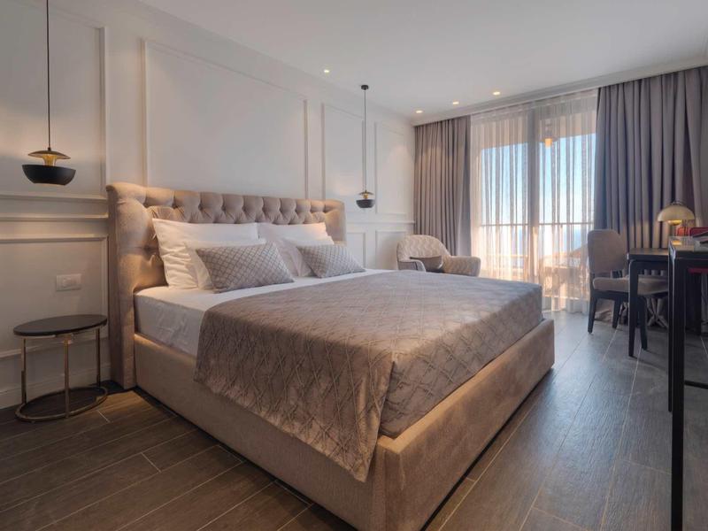 Langer Sandstrand mit Sonnenliegen, klarem blauem Meer und bewaldeten Hügeln im Hintergrund.