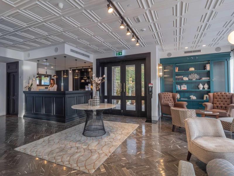 Modernes, helles Café mit schwarzer Bar, blauen Regalen, gemütlichen Sesseln und großem Teppich.