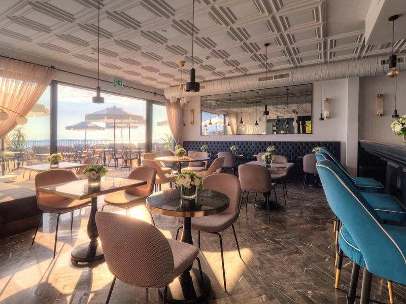 Helles Café mit gemustertem Boden, runden Tischen, bequemen Stühlen und großen Fenstern mit Aussicht.