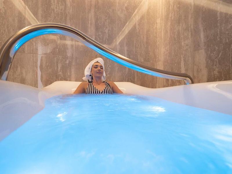 Ein Frau entspannt sich in einem Whirlpool mit blauem Wasser und grauen Wänden im Hintergrund.