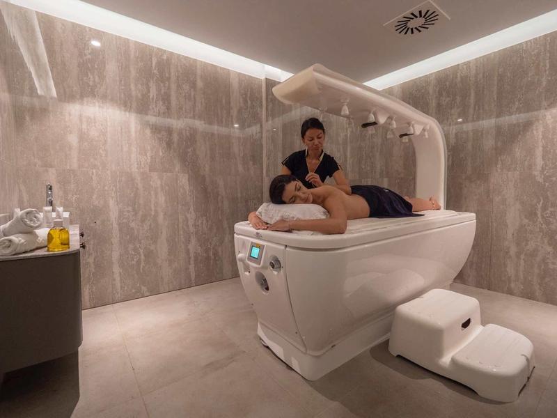 Moderner Wellnessraum mit grauen Wänden, Massagewanne und einer Person, die Massage gibt.