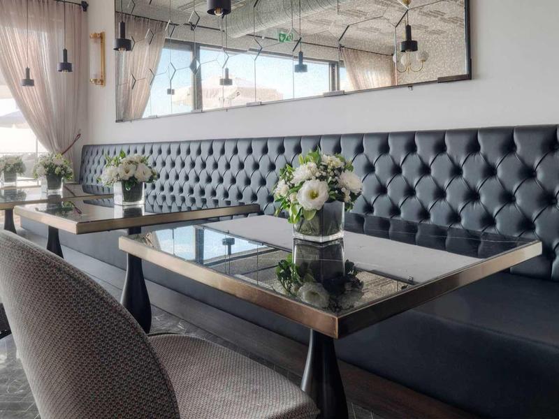 Elegantes Wohnzimmer mit blauer Ledercouch, Glas-Couchtisch und rosa Vorhängen, heller Raum.