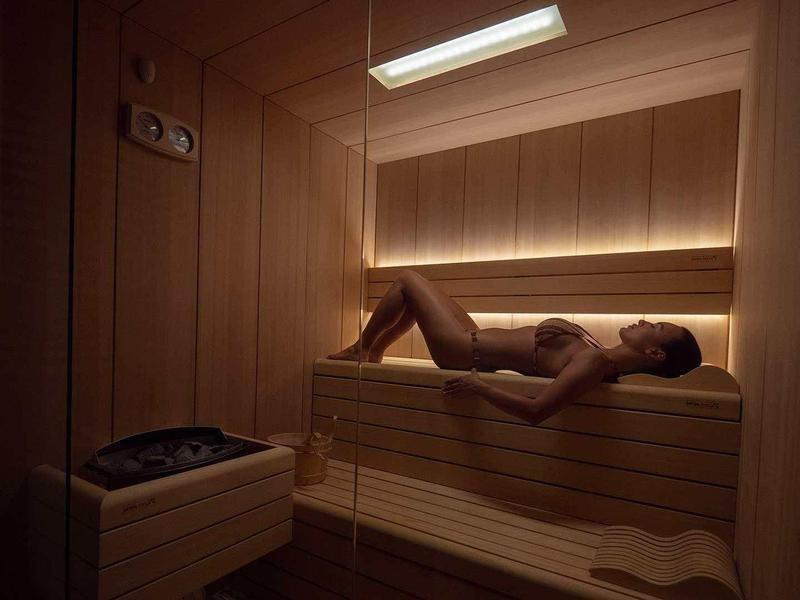 Mann liegt entspannt auf Holzbank in warmer, gedämpfter Sauna mit indirekter Beleuchtung.