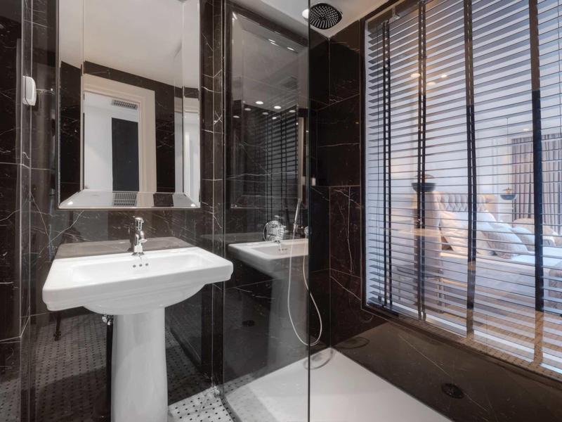 Modernes Badezimmer mit hellem Waschbecken, Glas-Dusche und großen Fensterläden aus Holz.