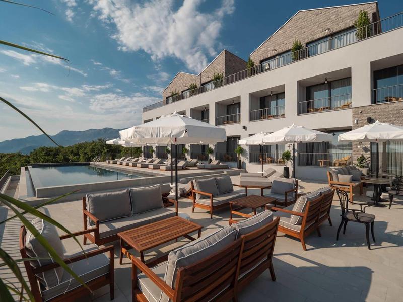 Terrasse mit Holzmöbeln, Sonnenschirmen und Panoramablick auf Berge bei sonnigem Himmel.
