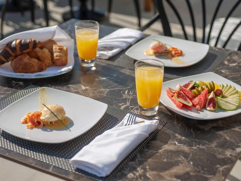 Tisch mit Marmorplatte, belegte Teller, Croissants, zwei Orangensäfte und weiße Servietten.
