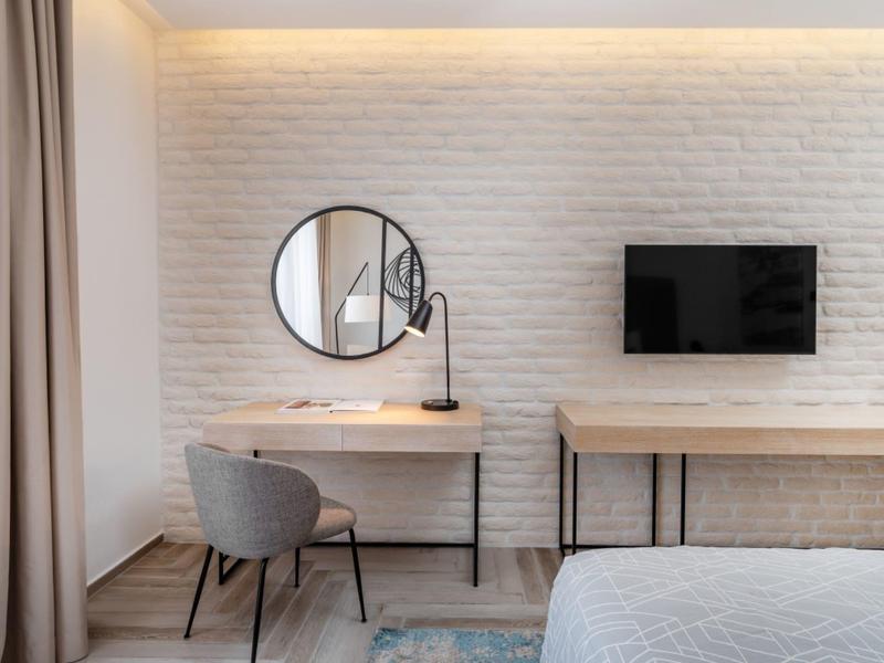 Chambre d'hôtel moderne avec bureau, miroir rond, chaise et télévision murale.