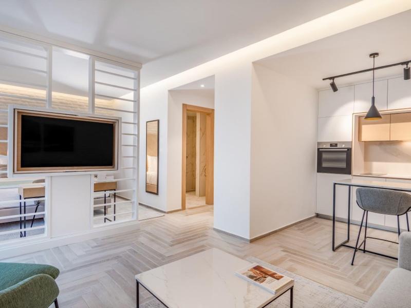 Espace de vie moderne avec meuble TV blanc, coin repas et cuisine ouverte avec tabourets de bar.