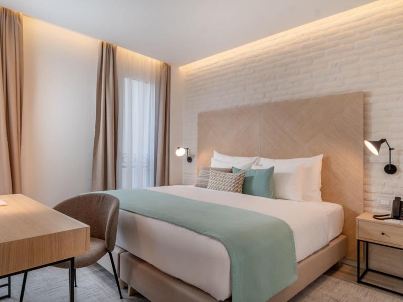 Chambre d'hôtel moderne avec grand lit, bureau et lumière douce.