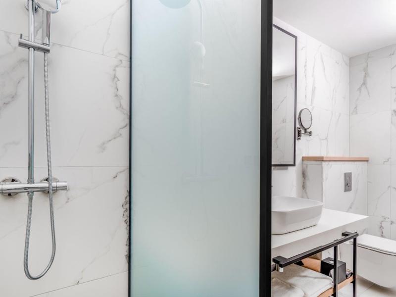 Salle de bain moderne avec douche, lavabo et toilettes en aspect marbre blanc.