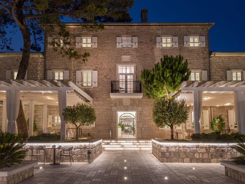 Bâtiment éclairé avec murs en pierre, arbres et espaces assis couverts la nuit
