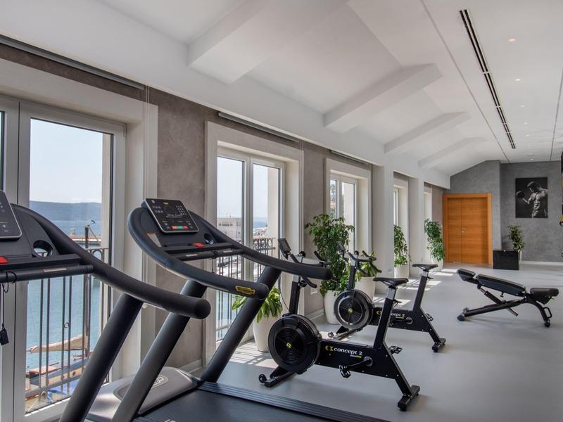 Salle de sport lumineuse avec tapis roulants et appareils d'exercice avec vue sur l'eau.
