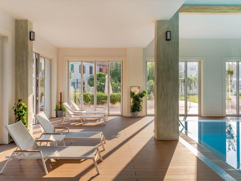 Piscine intérieure lumineuse avec chaises longues confortables et vue sur le jardin avec parasols.