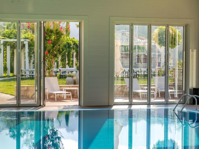 Piscine intérieure donnant sur un jardin ensoleillé avec des sièges et une végétation luxuriante.
