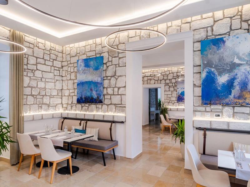 Restaurant lumineux avec murs en pierres blanches, mobilier moderne et œuvre d'art abstraite bleue.