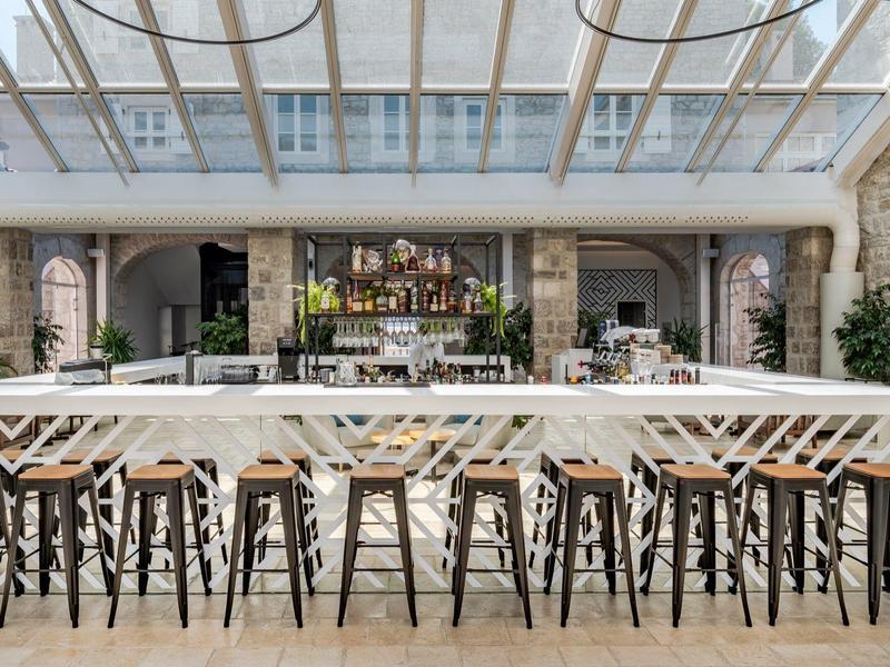 Espace bar d'hôtel moderne avec tabourets en bois et métal sous un toit en verre.