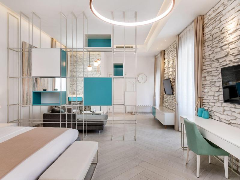 Chambre d'hôtel moderne avec lignes épurées, mur en pierre, espace de travail et coin salon.