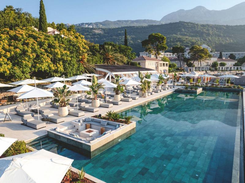 Espace piscine moderne avec chaises longues et parasols blancs devant un paysage montagneux.