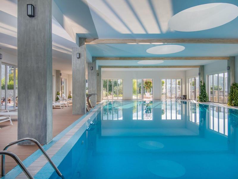 Piscine intérieure lumineuse avec grandes fenêtres et lumière du soleil par des ouvertures au plafond.