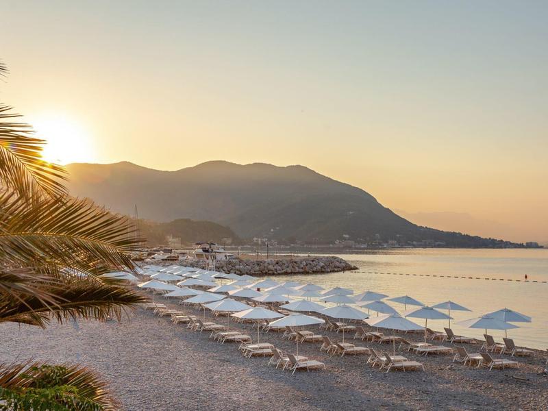 Coucher de soleil sur une plage calme avec chaises longues et parasols près des palmiers.