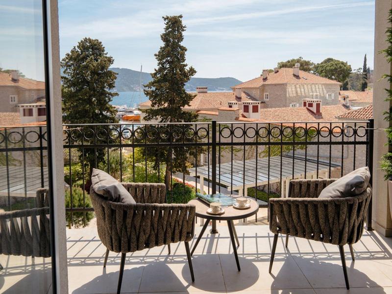 Balcon avec deux chaises et table donnant sur l'eau, les arbres et les maisons sous un ciel clair.