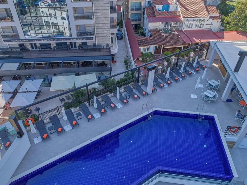 Großer blauer Pool mit rechteckiger Form auf Dachterrasse, umgeben von Liegestühlen und Sonnenschirmen.