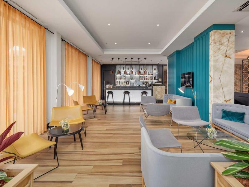 Moderner Lounge-Bereich mit hellen Sesseln, Holzfußboden, großen Fenstern und elegantem Tresen.