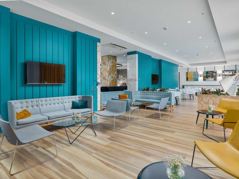 Modern eingerichteter Wartebereich mit türkisfarbenen Wänden, grauen Sofas und Holzboden.