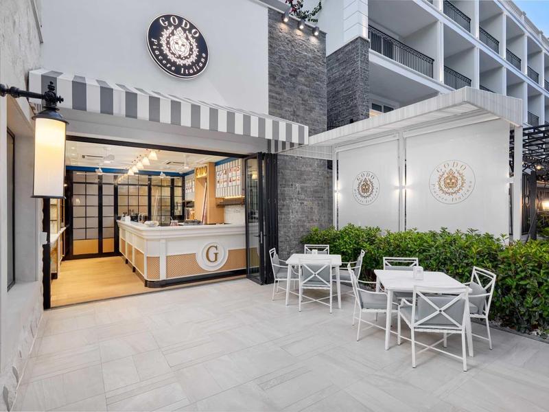 Moderner Café-Außenbereich mit weißen Stühlen, Tischen und großem Eingangsbereich, helle Gestaltung.