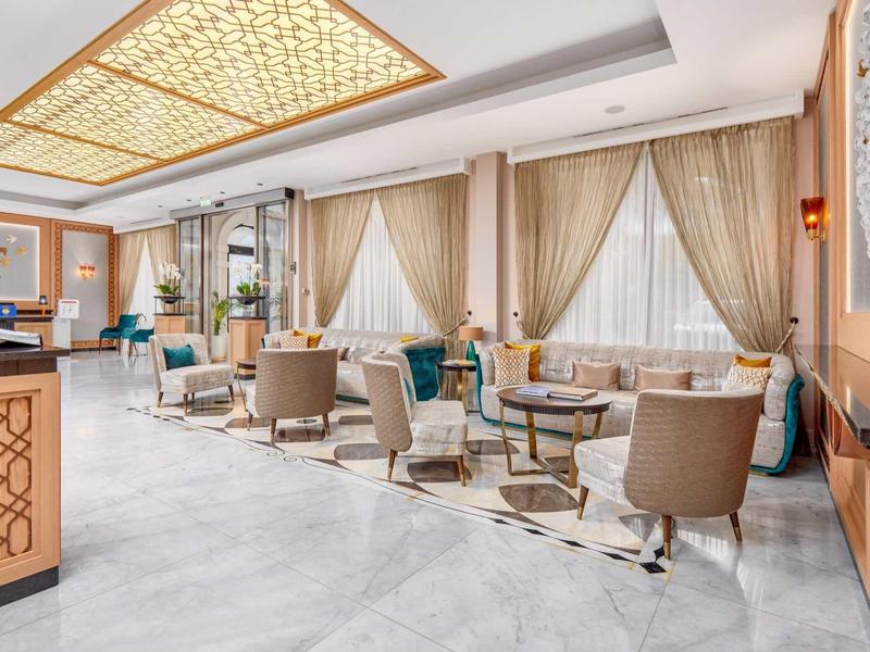 Eleganter Aufenthaltsraum mit beigen Sesseln, großen Fenstern, Vorhängen und hellem Marmorfußboden.