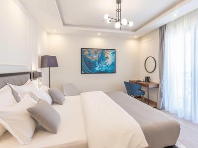 Modernes Schlafzimmer mit großem Bett, grauen Kissen, Schreibtisch und hellem Tageslicht durch Fenster.