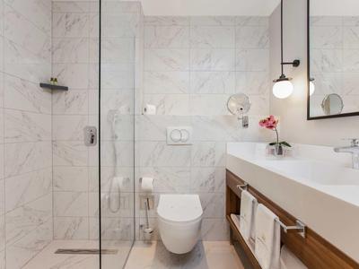 Modern gestaltetes Badezimmer mit Glasdusche, Wand-WC, großem Spiegel und Holzunterschrank.