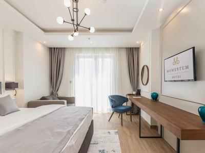 Modern eingerichtetes Schlafzimmer mit Doppelbett, Schreibtisch, Sesseln und großem Fenster mit Vorhängen.