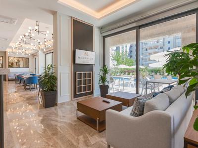 Lounge moderna dell'hotel con comodi divani, tavoli in legno e vista su una terrazza esterna con posti a sedere.