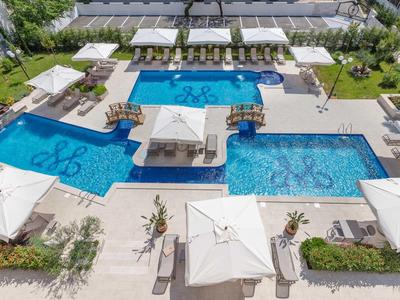 Area piscina esterna moderna con più piscine, ombrelloni e lettini in un hotel resort.