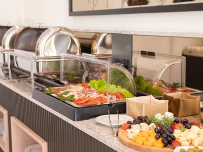 Buffet mit verschiedenen warmen Speisen und frischem Obst auf einem langen Tisch in modernem Raum.