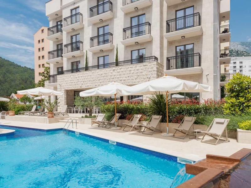 Mehrstöckiges Hotel mit blauen Glasbalkonen, Pool und Sonnenschirmen vor bewölktem Himmel.